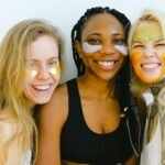 Group of women with masks and patches smiling while looking at camera and laughing during skincare procedure in studio on weekend