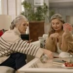 Two senior women enjoying a card game in a warmly decorated living room.