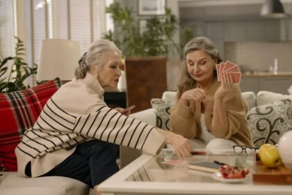 Two senior women enjoying a card game in a warmly decorated living room.